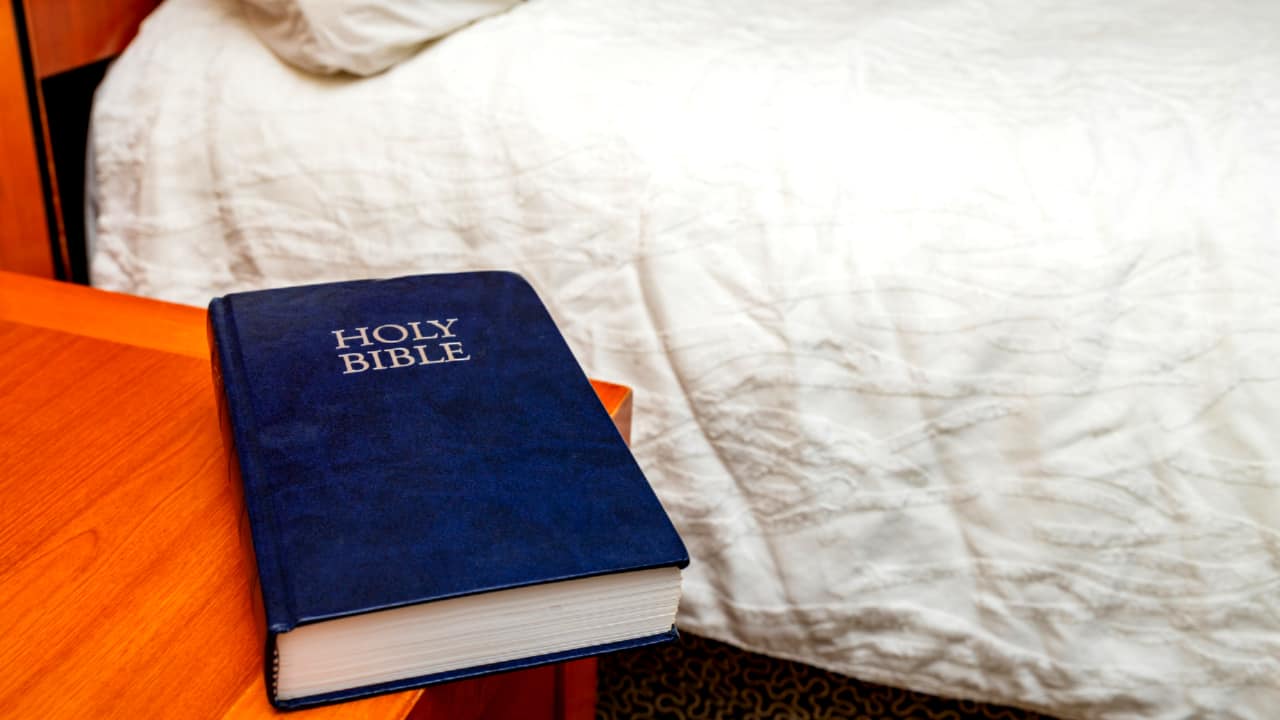 A hotel bible on a wooden bedside table.