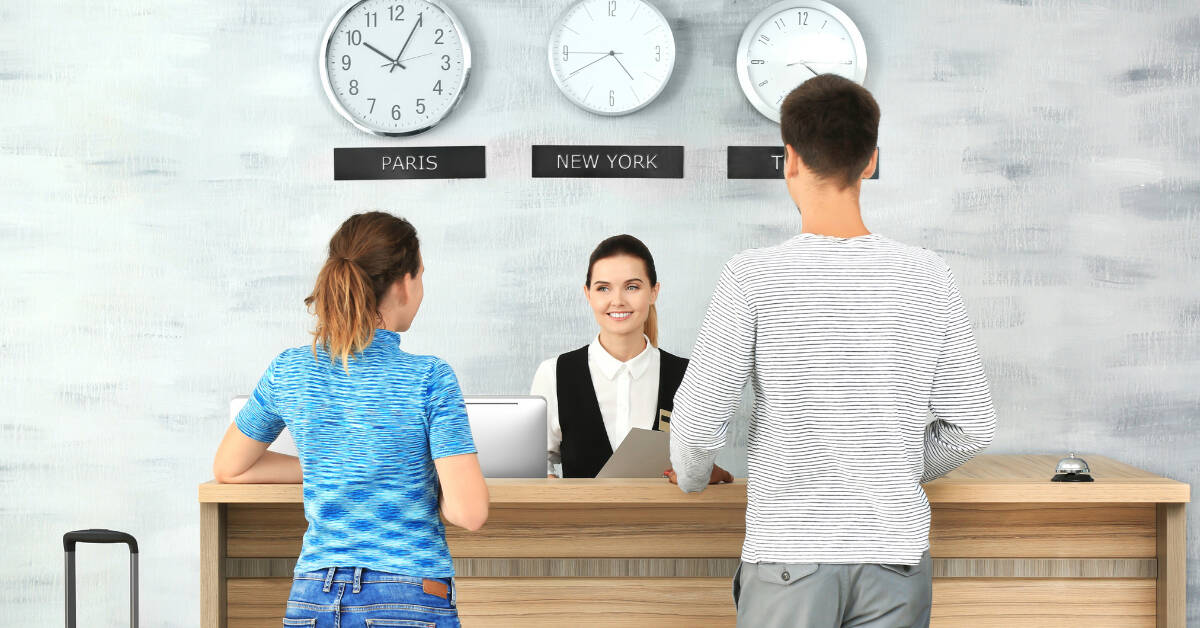 Two individuals inquiring about the age requirement to book a hotel room at the reception desk.